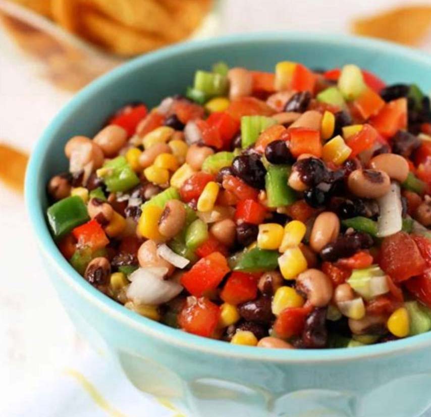 A vibrant bowl of Texas caviar salad featuring black-eyed peas, black beans, corn, diced tomatoes, green bell peppers, and onions, all mixed together in a light blue bowl. Perfect for a colorful and fresh dish.